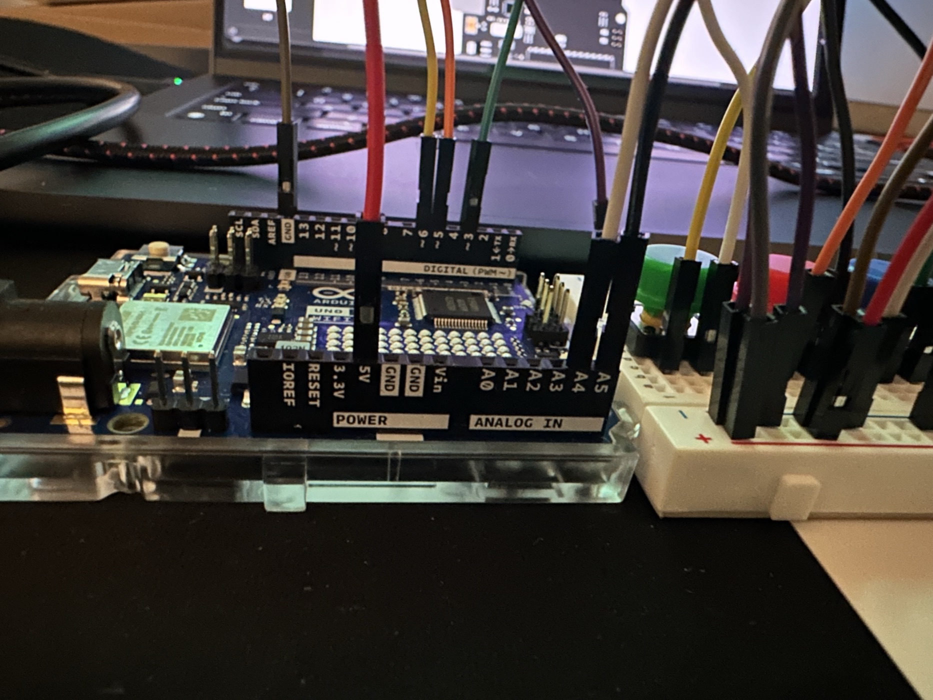 An Arduino UNO wired up on a breadboard with jumper wires running off-frame in front of a laptop.